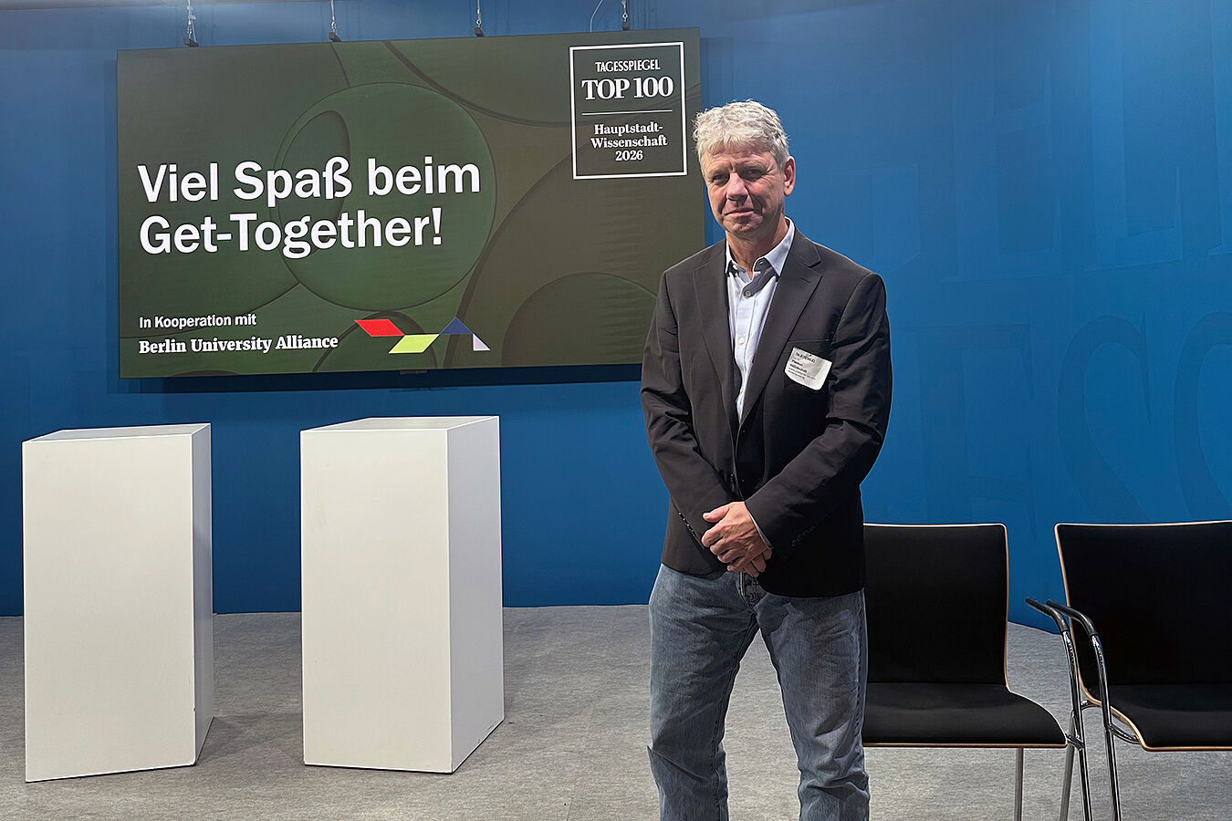 Prof. Hildebrandt steht in grauer Jeans, mit schwarzem Jackett und hellem Hemd auf einer Bühne. Hinter ihm ein Schild, auf dem steht: Tagesspiegel TOP 100 - Hauptstadt-Wissenschaft 2026